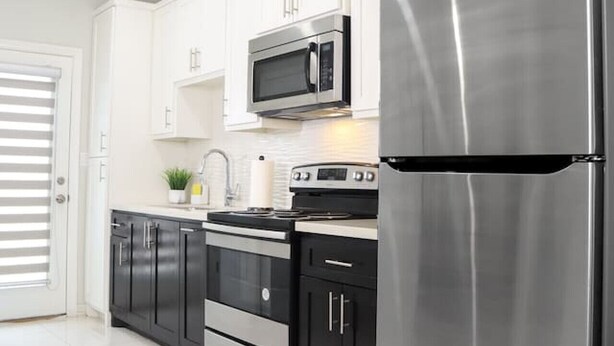Una cocina moderna con armarios blancos, electrodomésticos de acero inoxidable y un refrigerador negro.