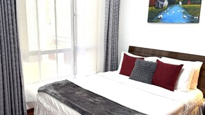 Un dormitorio con una cama grande, un cuadro de un paisaje fluvial y vistas de un edificio a través de la ventana.