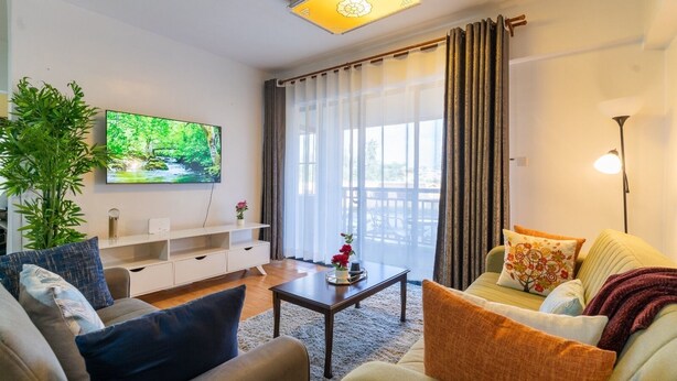 Una sala de estar con televisor, sofá, mesa de centro y un amplio ventanal con cortinas.