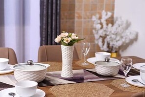 Una mesa de comedor dispuesta con vajilla de cerámica blanca, un florero con flores y una copa de vino.