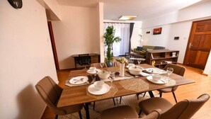 Un comedor con una mesa de madera dispuesta para seis personas, rodeada por seis sillas. Hay una planta en maceta sobre la mesa, y se ve un sofá al fondo.