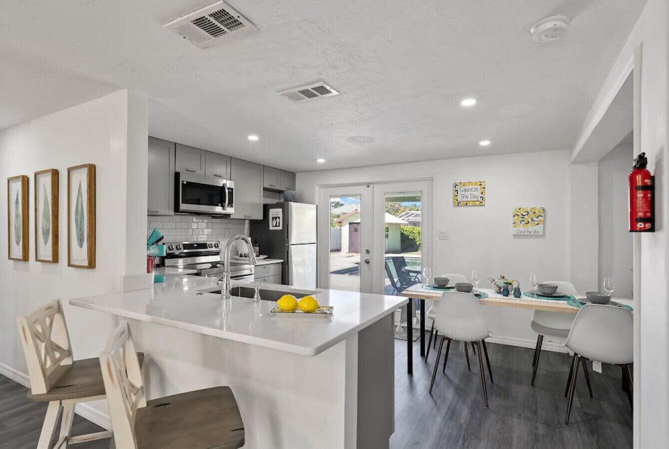 A modern kitchen with a central island, white cabinetry, and a dining area with a view.