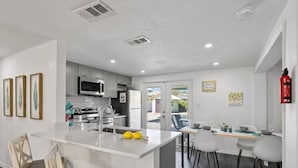 A modern kitchen with a central island, white cabinetry, and a dining area with a view.
