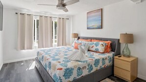 A bedroom with a bed, a ceiling fan, a nightstand, and a painting on the wall.