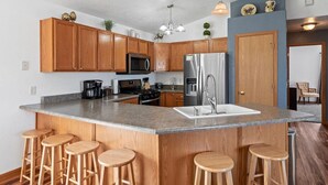 Une cuisine moderne avec des meubles en bois, un réfrigérateur en acier inoxydable, un plan de travail en granit et un coin bar avec des tabourets.