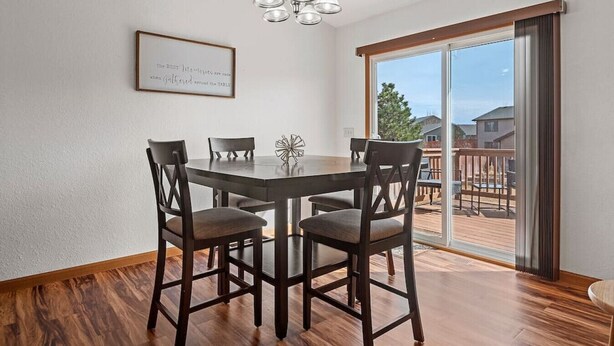 Un coin repas comprenant une table ronde, quatre chaises, un lustre et une porte-fenêtre coulissante donnant sur une terrasse extérieure.