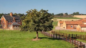 Un paysage rural avec un grand arbre, une maison en briques et une zone délimitée par une clôture.
