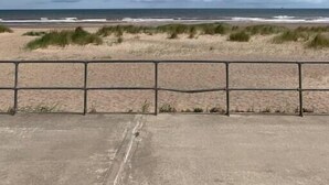 Une vue sur la plage avec une promenade en béton et une rambarde en métal.