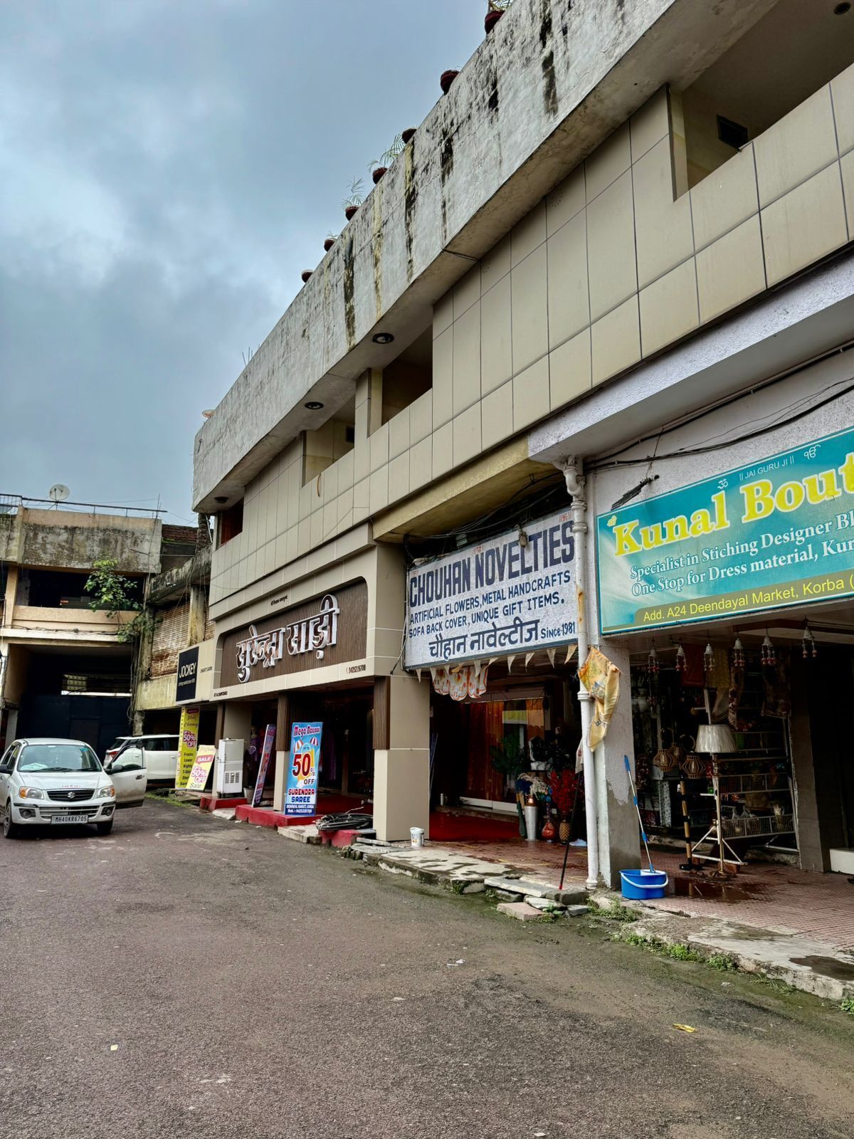 A street view with various shops, including one named 'Kunal Boutique' and another with a sign for 'Chouhan Novelties'.