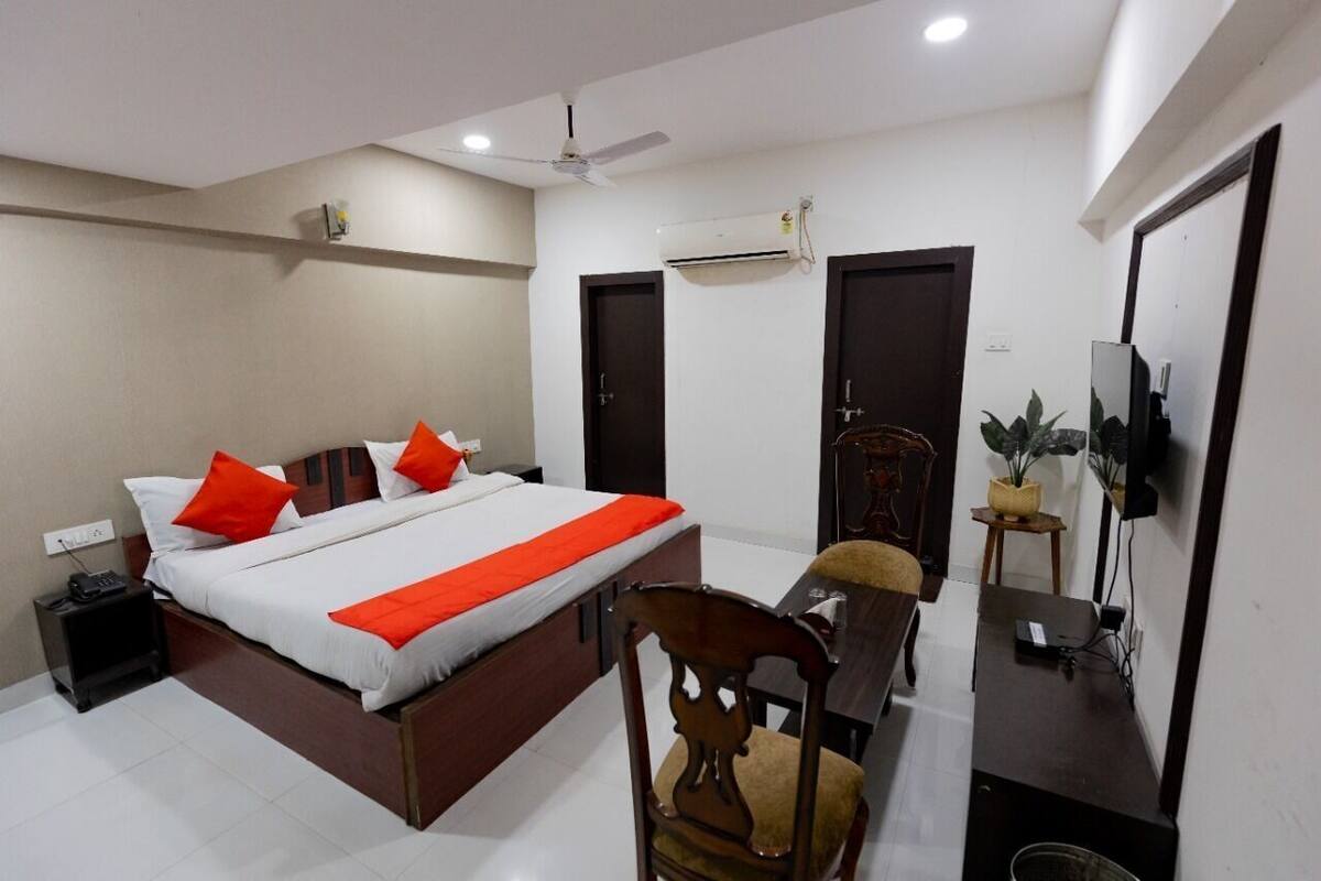 Una habitación de hotel con cama, escritorio, silla, televisor y aire acondicionado.