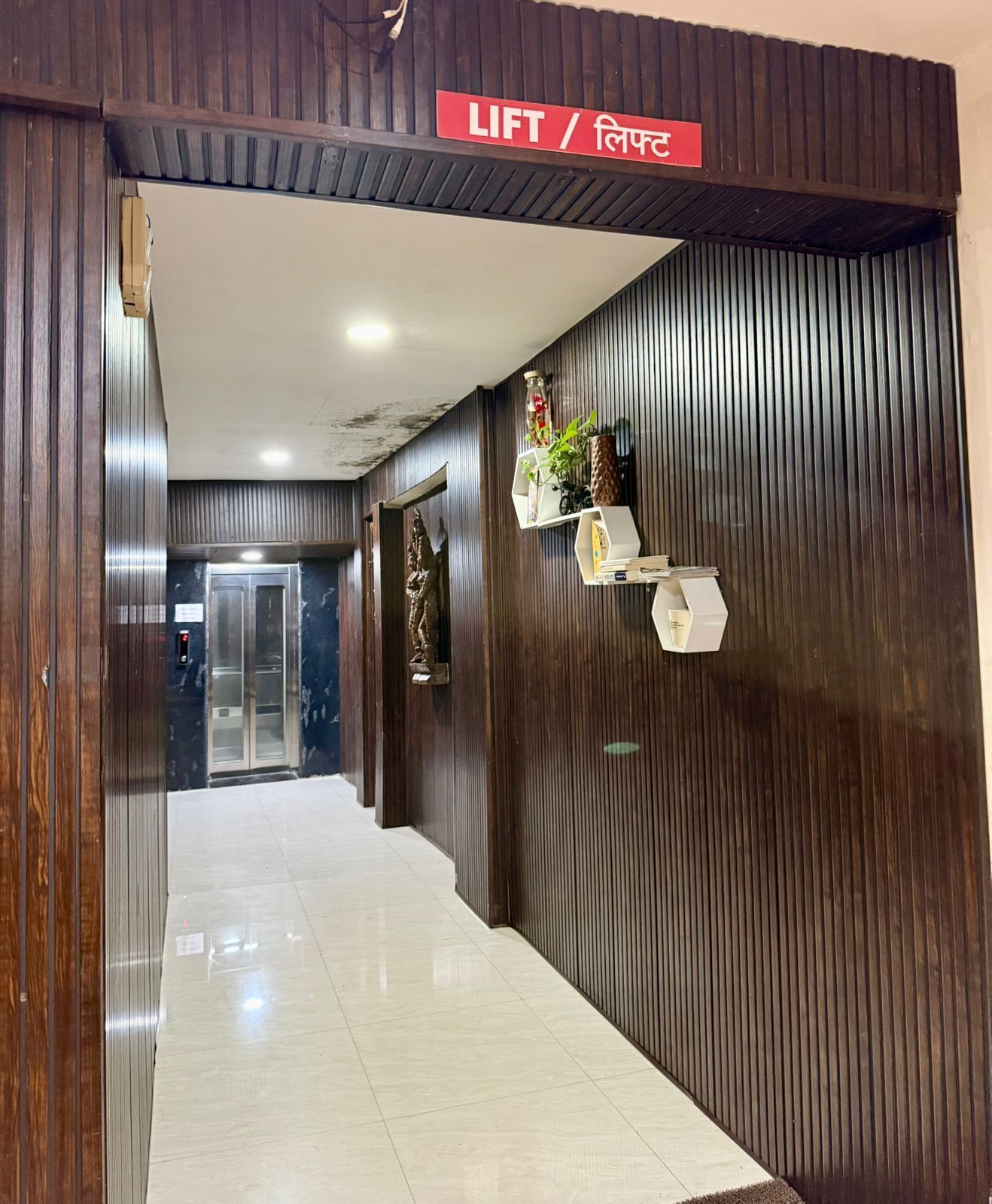 A hotel corridor with a lift, wooden paneling, and a tiled floor.