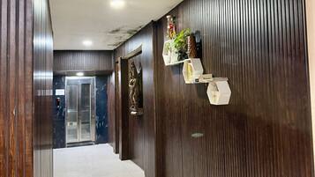 A hotel corridor with a lift, wooden paneling, and a tiled floor.