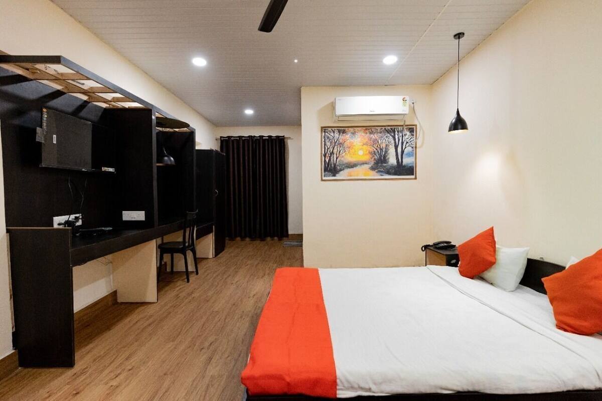 Una habitación de hotel con una cama, un escritorio con silla, aire acondicionado, un cuadro en la pared y un ventilador de techo.
