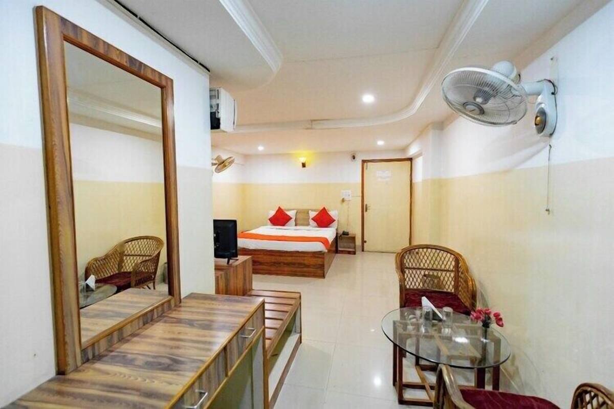 Habitación de hotel con cama, escritorio y silla, espejo, ventilador de pared y una pequeña mesa con una silla.