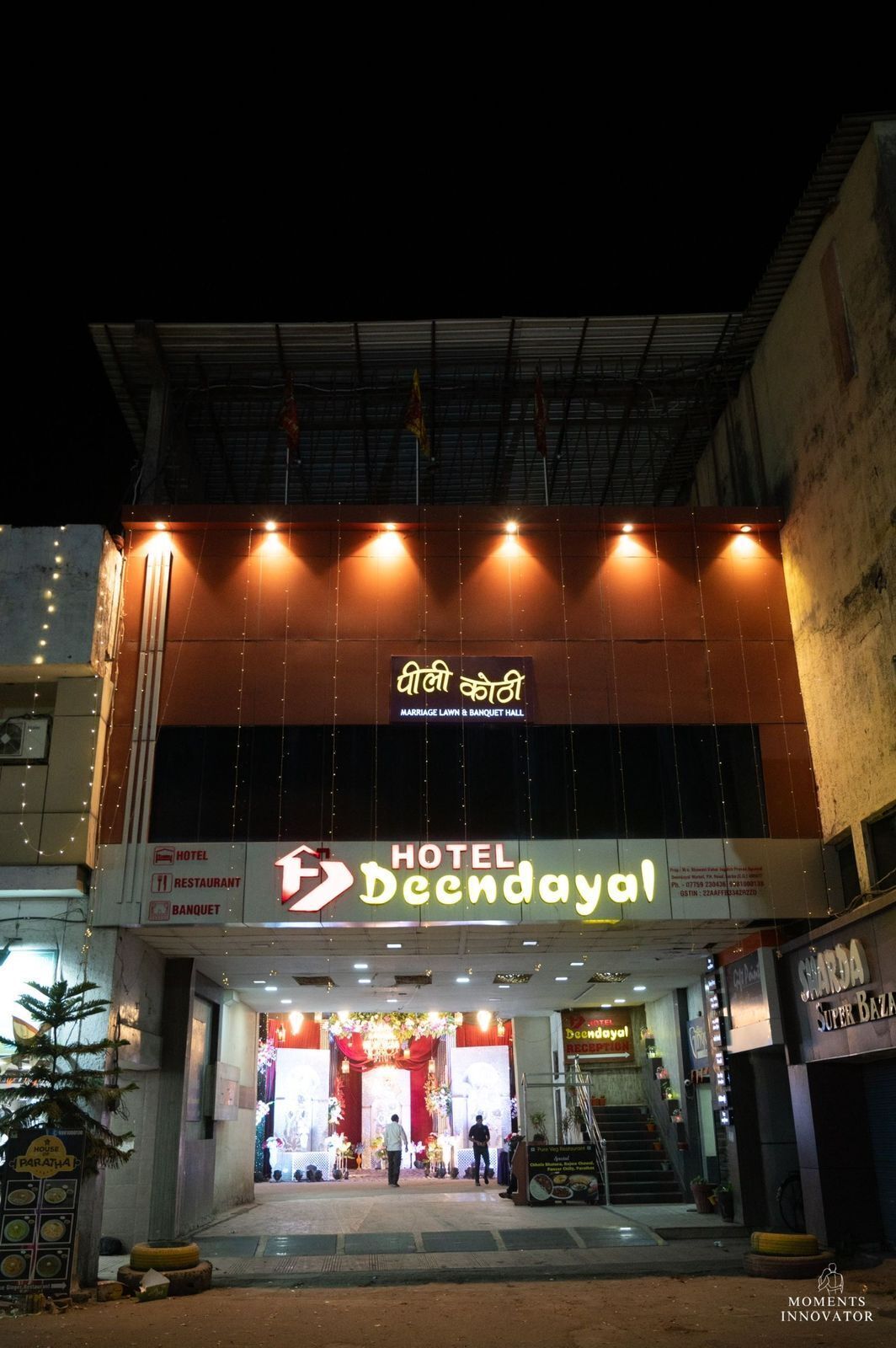 L’entrée d’un hôtel, avec une enseigne indiquant « Hôtel Deendayal », comprenant un espace de réception et une scène pour les événements.
