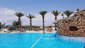 Ein Schwimmbecken mit klarem, blauem Wasser, umgeben von Palmen und einer Felsformation.