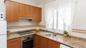 Eine kleine Küche mit Holzausstattung, einem eingebauten Backofen, einer Spüle und einem Fenster mit transparenten Vorhängen.