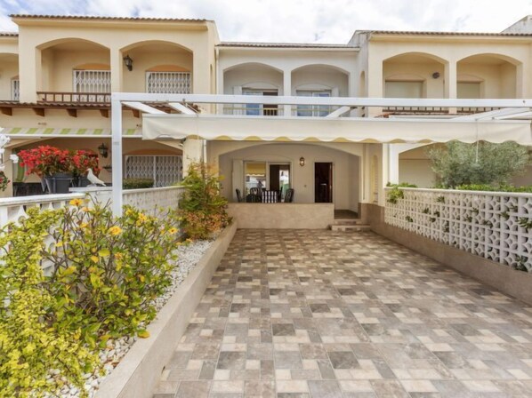 A courtyard with a tiled floor, surrounded by a white fence and potted plants.