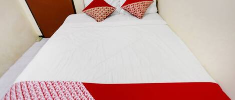 A bed with white bedding and two red pillows with a pattern.