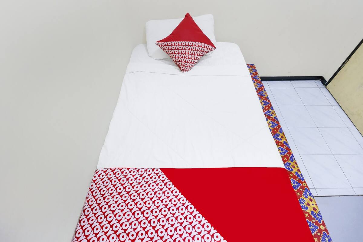 A single bed with a white and red bedspread, a red pillow, and a patterned border.