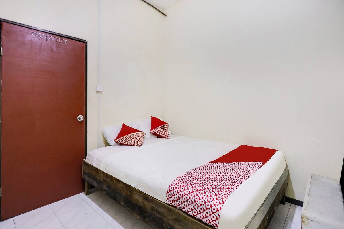 A single bed with a wooden frame, white bedding, and red and white patterned pillows.