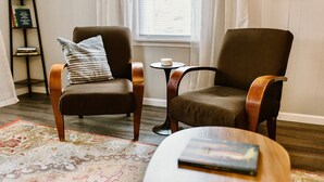 Un salon avec deux fauteuils, une petite table ronde, un tapis à motifs et une bibliothèque remplie de livres.