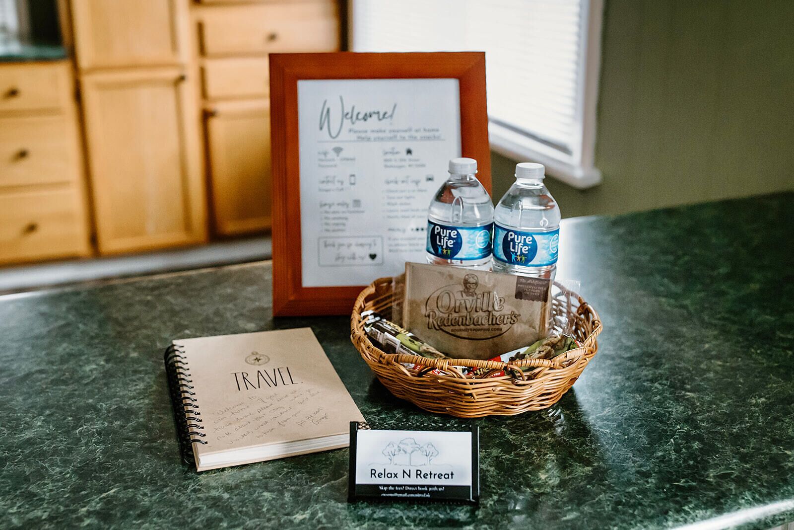 A travel notebook, a welcome sign, a basket with water bottles and a bag of snacks, and a sign for a retreat.