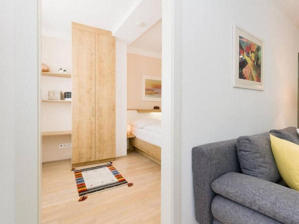 A modern room with a wooden wardrobe, a bed, a gray sofa, and a colorful rug.