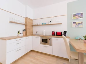 A compact kitchen with white cabinets, a microwave, a coffee maker, and a wooden countertop.