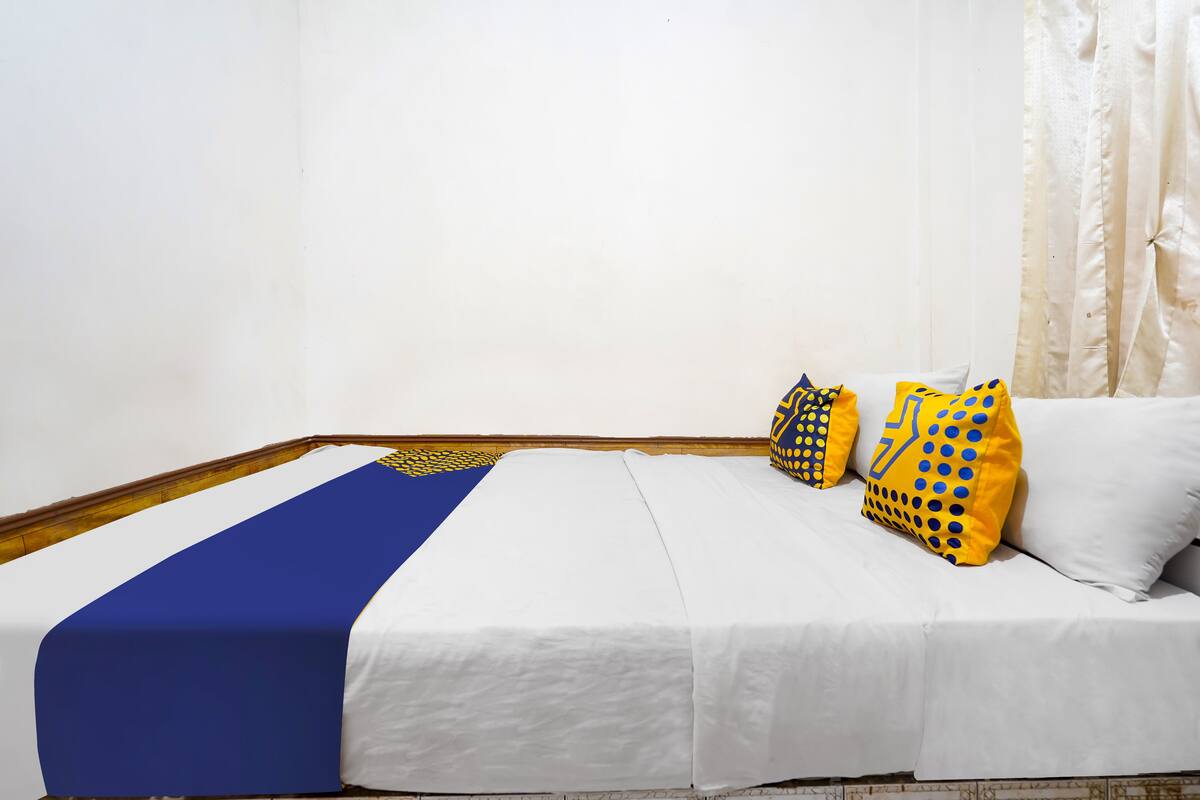 Un lit simple avec une couvre-lit bleue et blanche, deux oreillers jaunes à motifs bleus et un oreiller blanc.