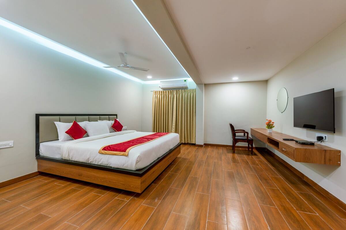 A modern hotel room with a wooden bed, a desk with a TV, and a ceiling fan.