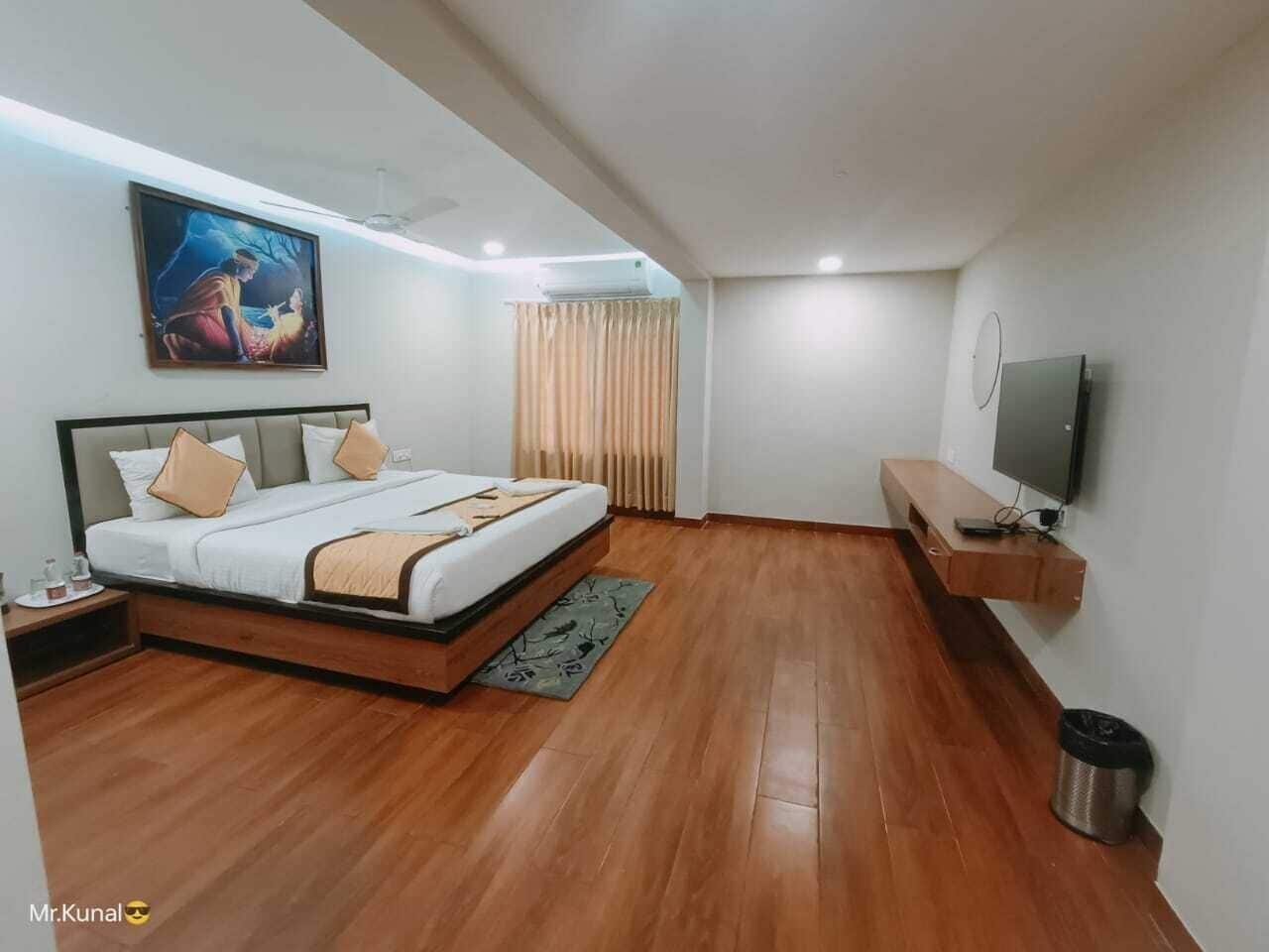Een moderne hotelkamer met een houten vloer, een bed met beige en witte beddengoed, een wandgemonteerde televisie en een schilderij aan de muur.