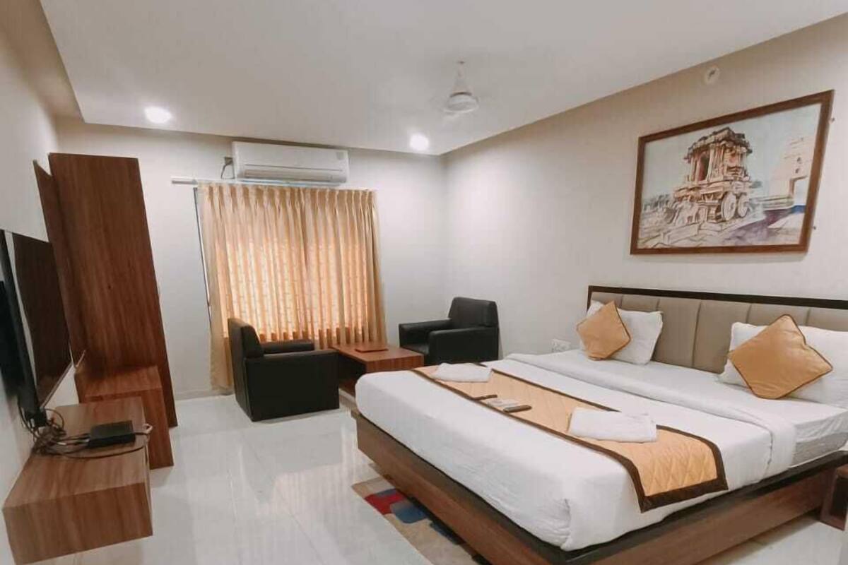 A modern hotel room with a large bed, a desk, a chair, and a television.