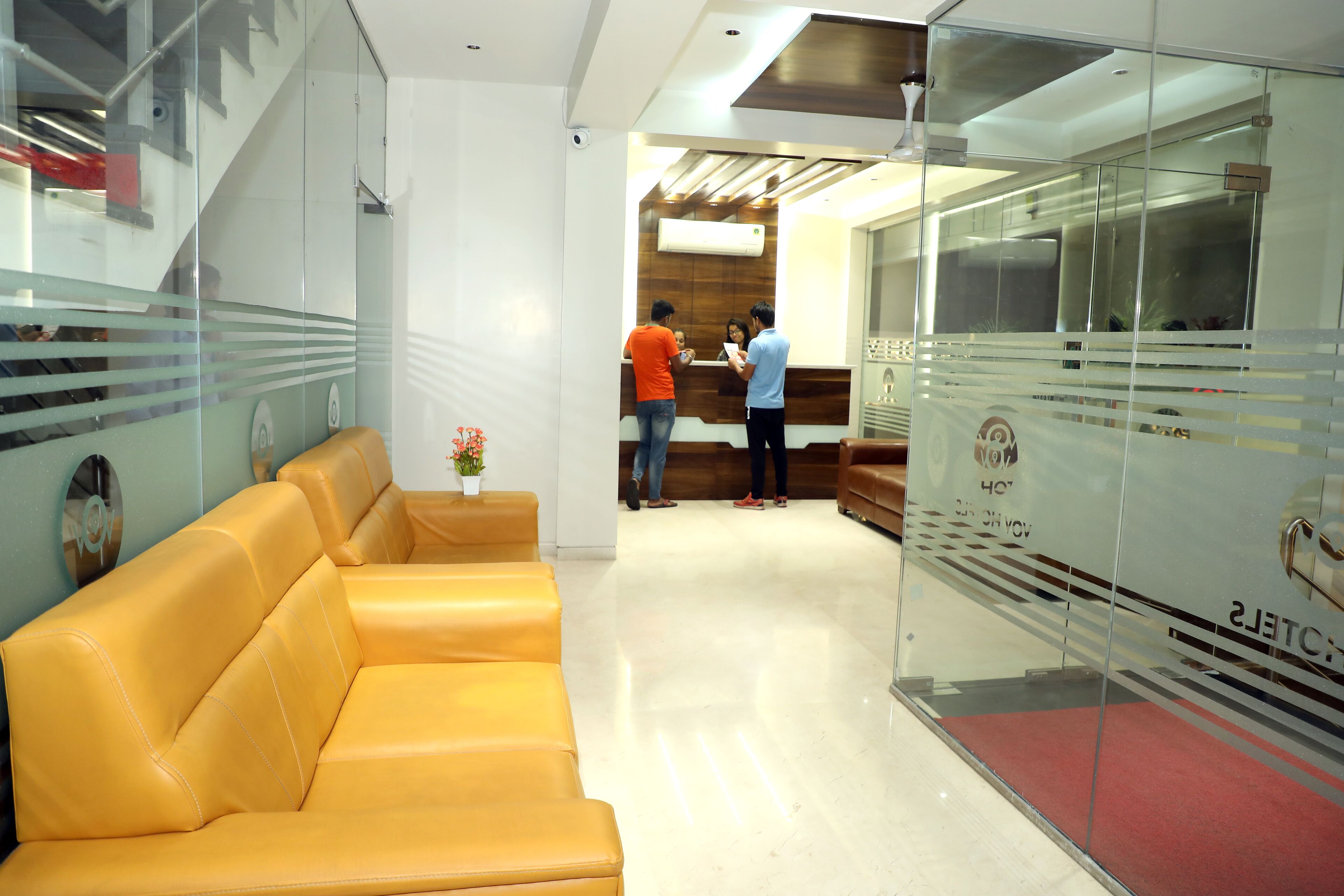 A reception area with a yellow leather sofa, a reception desk, and a glass wall with a red carpet.