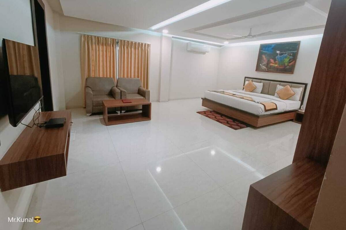 A modern hotel room with a flat-screen TV, a sofa, a bed with a wooden headboard, and a painting on the wall.