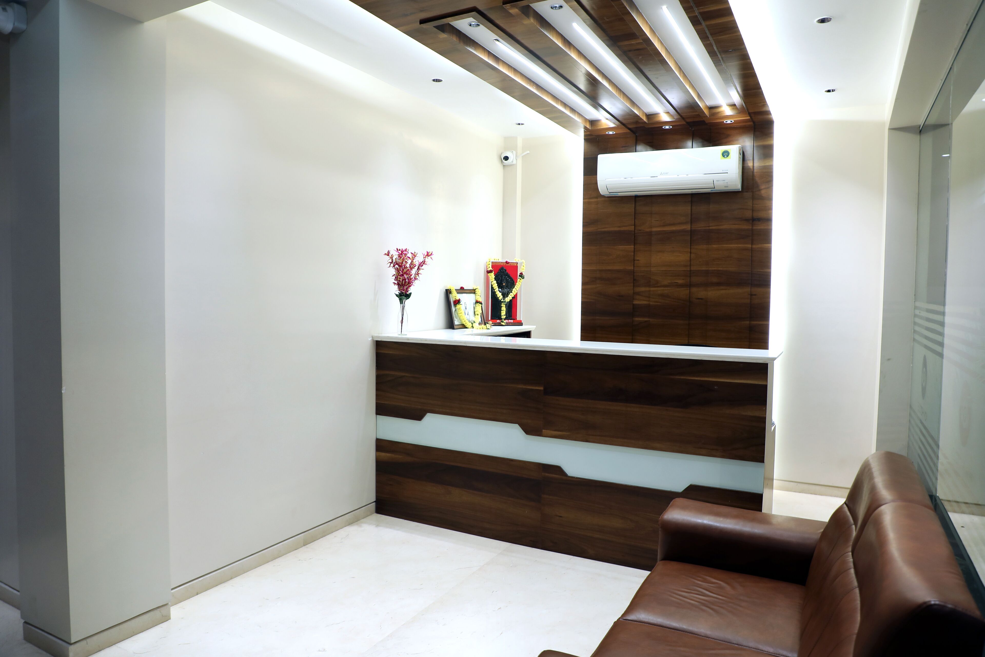 A modern reception area with a wooden reception desk, a brown leather sofa, and an air conditioning unit on the wall.