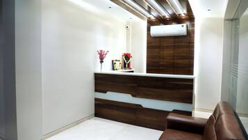 A modern reception area with a wooden reception desk, a brown leather sofa, and an air conditioning unit on the wall.