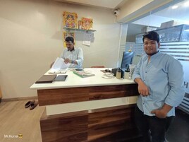 Un mostrador de recepción con acabado de madera y superficie blanca. Dos personas están detrás del mostrador, una de ellas parece ser la recepcionista.