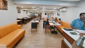 A spacious restaurant with wooden tables and orange cushioned seating. - VOV Hotels Vijayapura (Bijapur)