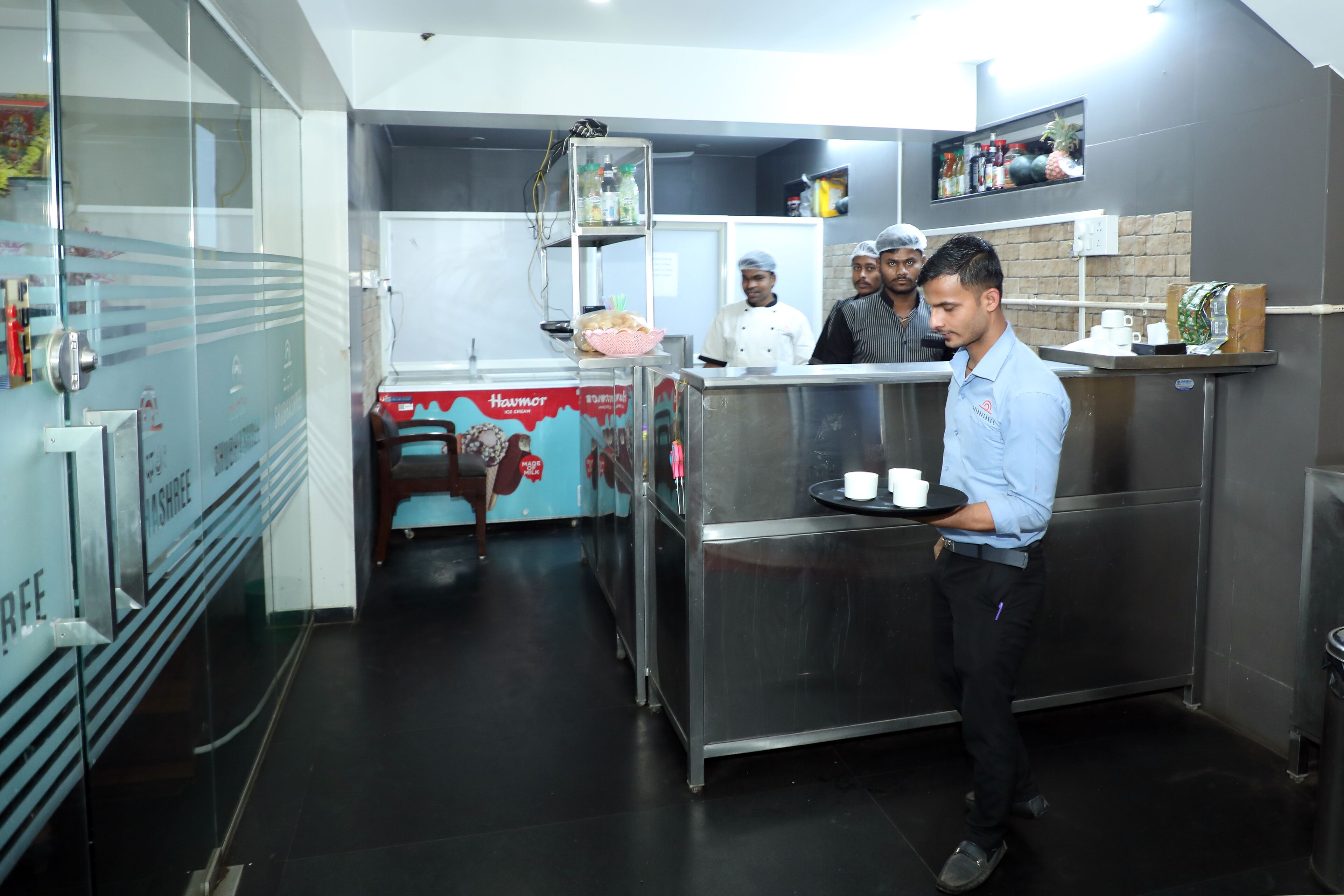 A kitchen area with stainless steel appliances, a glass partition, and a counter with a tray of items.