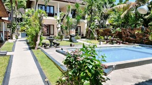A pool area with a stone pathway, a seating area, and lush greenery. - Rising Star Dive Resort (Karangasem)
