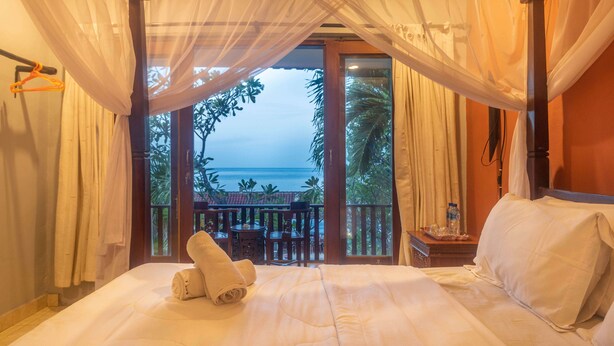 A bedroom with a bed, a nightstand, and a view of the ocean. - Rising Star Dive Resort (Karangasem)