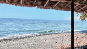 A beach with a thatched roof structure, pebbles, and the ocean. - Rising Star Dive Resort (Karangasem)