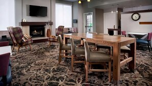 A modern hotel room with a large wooden dining table, comfortable seating, a fireplace, a flat-screen TV, and a clock on the wall. - Nautical Adventure Awaits in Annapolis Suites! Pets Allowed Here! Free Breakfast (Annapolis)