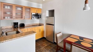 A compact kitchen with a granite countertop, stainless steel appliances, wooden cabinets, and a dining area with a table and chairs. - Nautical Adventure Awaits in Annapolis Suites! Pets Allowed Here! Free Breakfast (Annapolis)