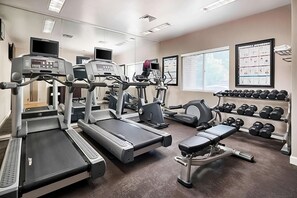 Ein Fitnessstudio mit Laufbändern, Krafttrainingsgeräten und einer Bank.