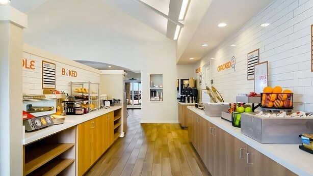 A modern kitchen with wooden cabinets, a coffee machine, and a display case with baked goods. - Nautical Adventure Awaits in Annapolis Suites! Pets Allowed Here! Free Breakfast (Annapolis)