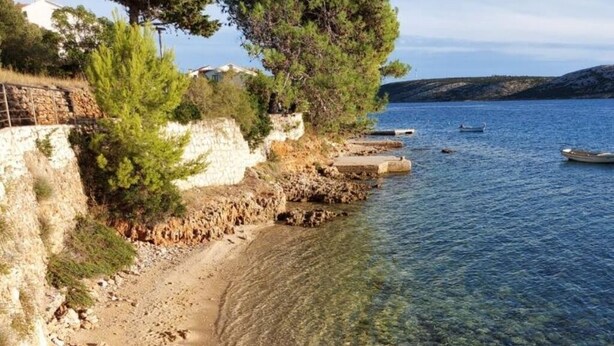 A clear beach with visible footprints, a stone wall, and a calm sea. - House in a quiet environment in the immediate vicinity  of the beach (Stara Novalja)