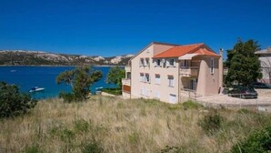 A building with a red roof, a balcony, and a view of a body of water and mountains. - House in a quiet environment in the immediate vicinity  of the beach (Stara Novalja)