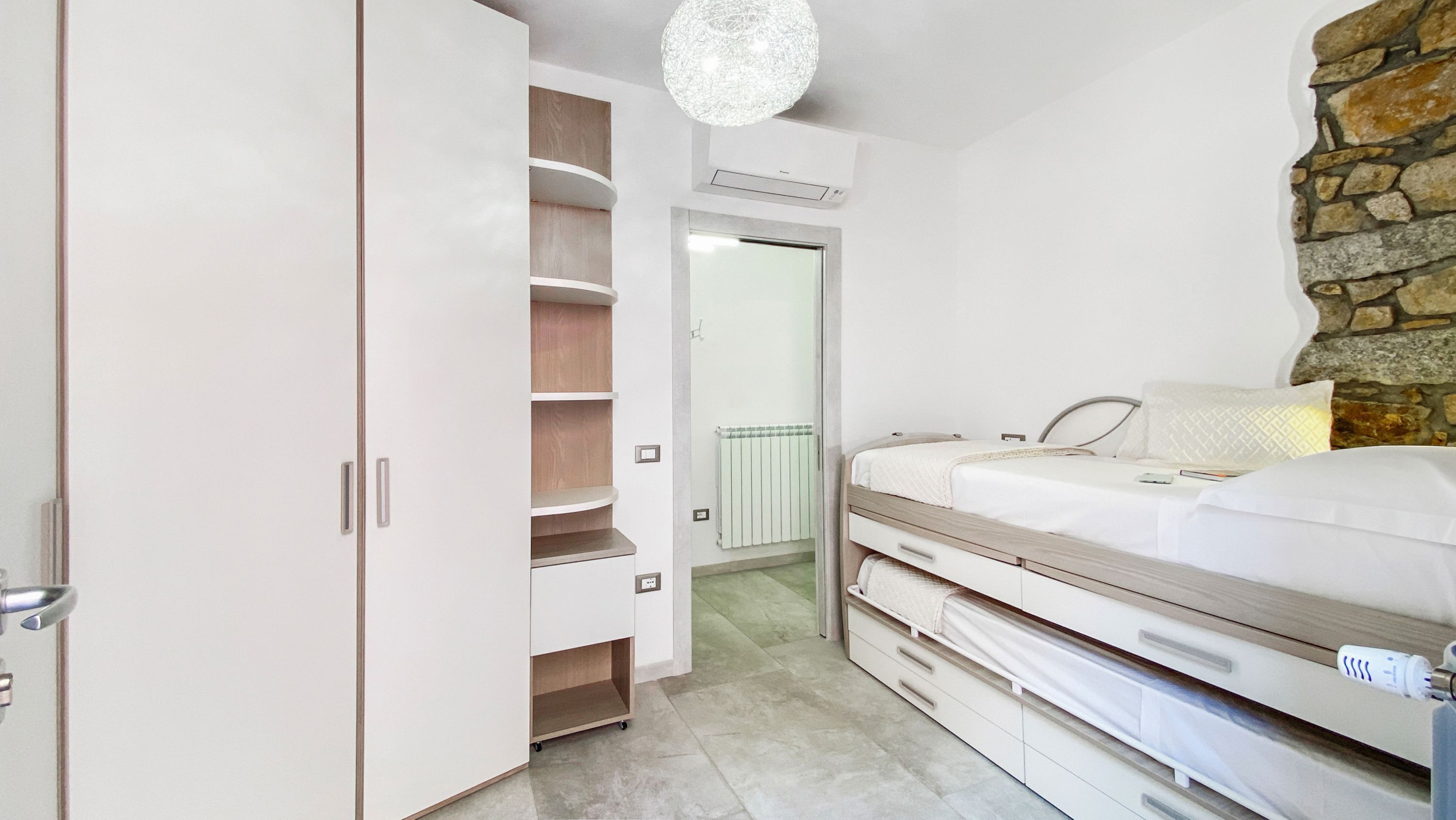A bedroom with a bed, a wardrobe, a mirror, and a stone wall.